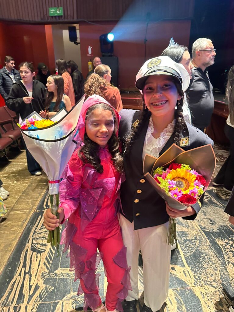 Two girls in costume holding flower bouquets at a theater event
