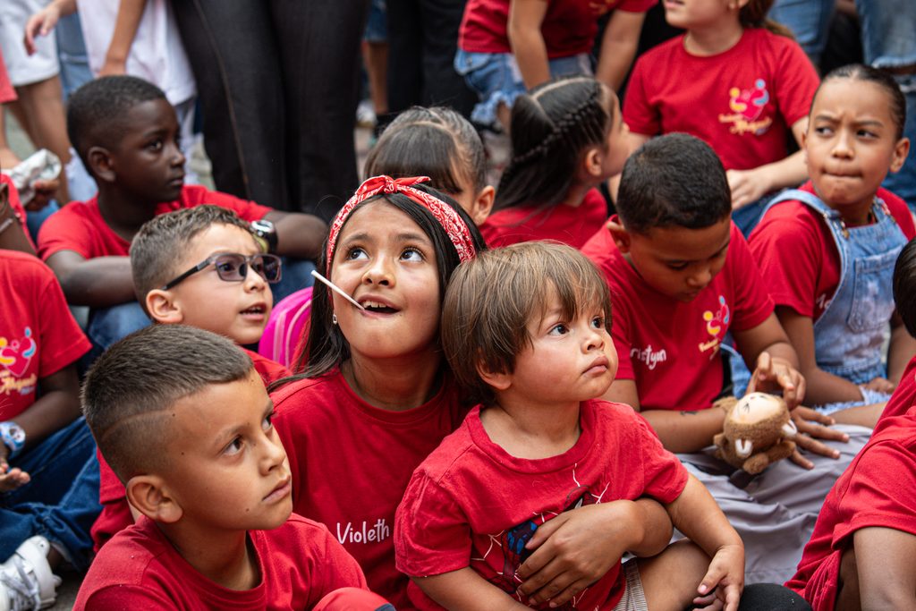 Group of children in red t-shirts gathered together at an outdoor community event