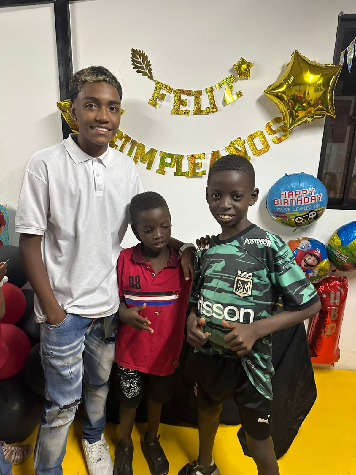 Three boys posing at a birthday party with a Feliz Cumpleaños banner