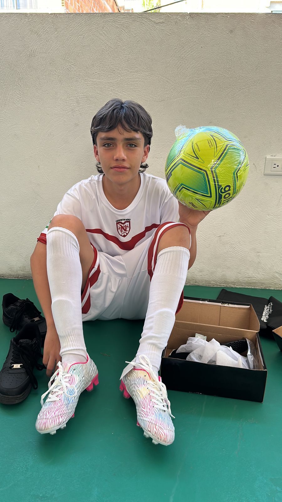 Young man sitting with a new soccer ball and new cleats beside him