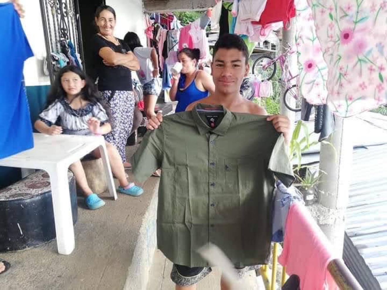 Young man holding up a donated shirt with family around