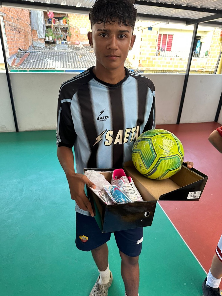 Young man in a soccer jersey holding a box with cleats and a soccer ball