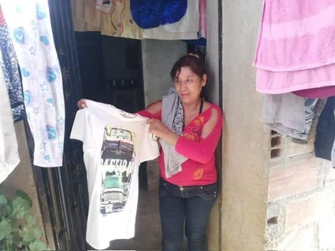 A mother holds up a donated shirt at her front door.